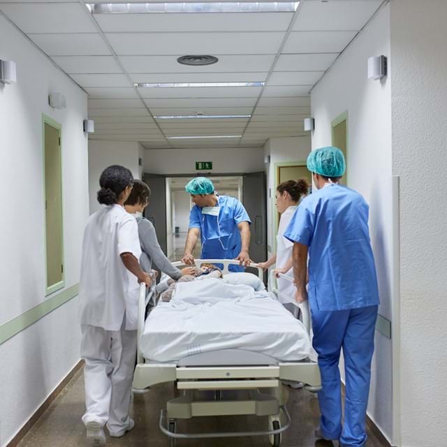medical team pushes patient on gurney down hallway